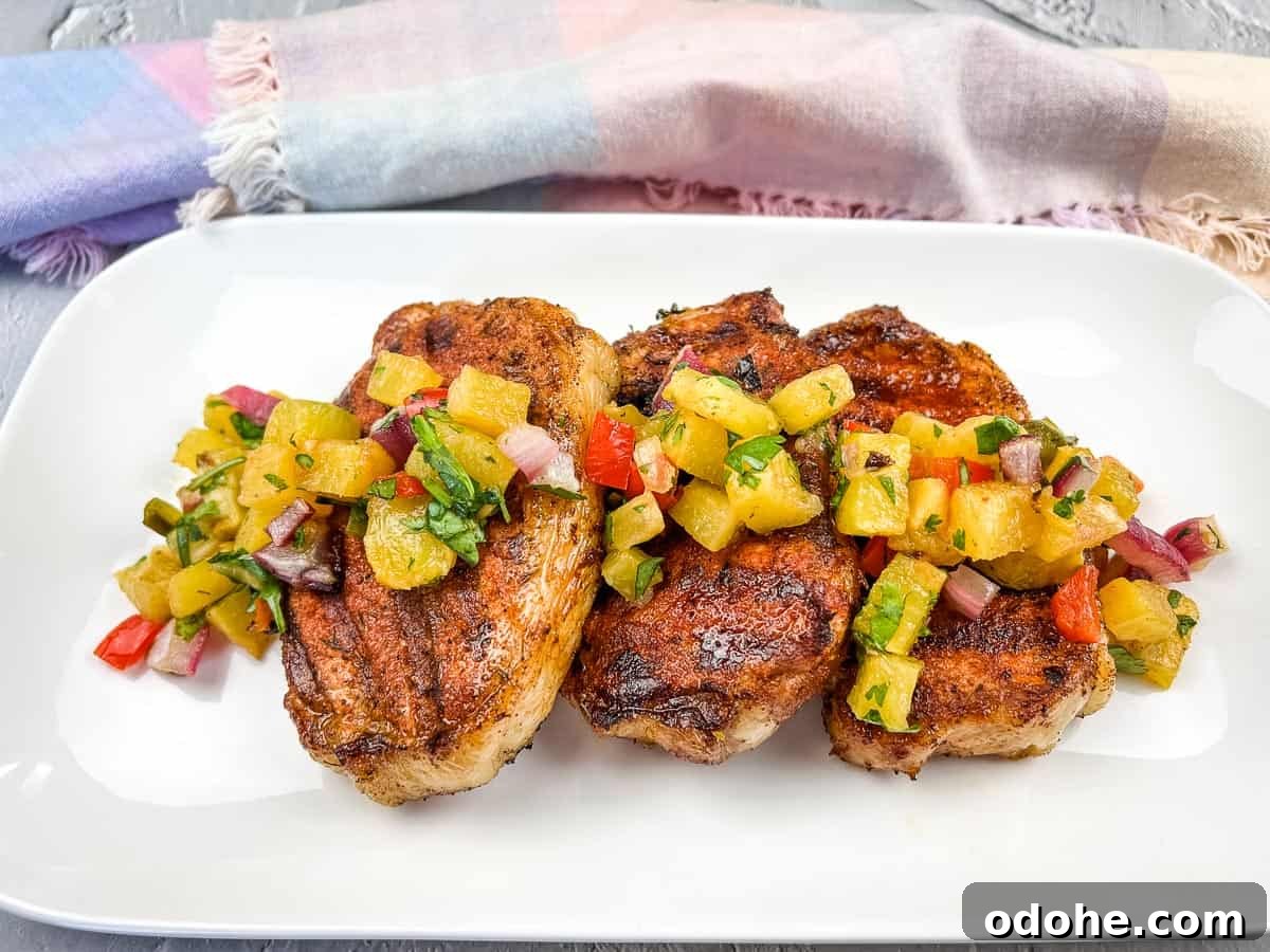 31 Memorial Day Recipes to Start Cookout Season Right 30 Grilled pork chops with pineapple salsa on a white plate.