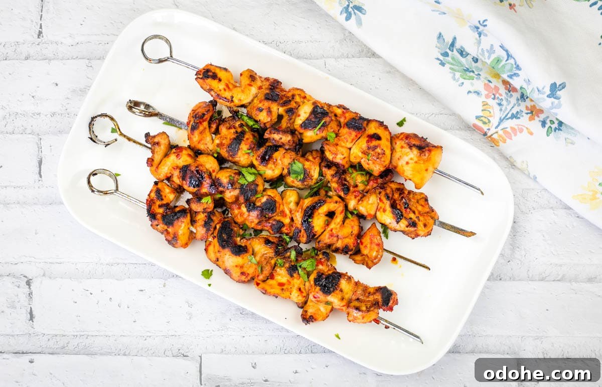 31 Memorial Day Recipes to Start Cookout Season Right 5 A rectangular white plate with four Sweet & Spicy Grilled Harissa-Honey Chicken Skewers garnished with chopped herbs.