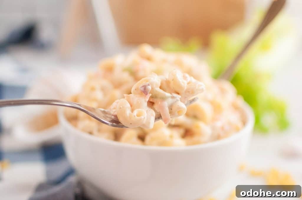 31 Memorial Day Recipes to Start Cookout Season Right 6 A close-up shot of a fork lifting a portion of macaroni salad, with a bowl of the salad in the blurred background.