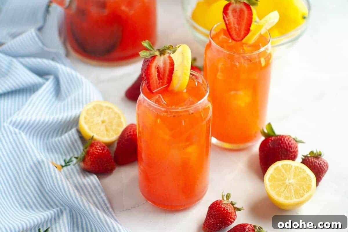 31 Memorial Day Recipes to Start Cookout Season Right 8 Two glasses of strawberry lemonade with ice, garnished with sliced strawberries and lemons, surrounded by fresh strawberries, lemon halves, and a blue striped cloth.