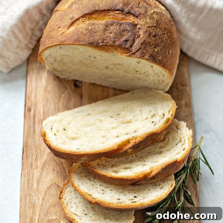 photo of rustic rosemary bread sliced on a cutting board with a sprig of fresh rosemary