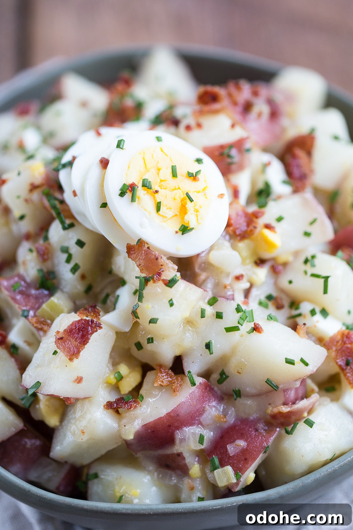 Authentic German Potato Salad with Hard-Boiled Eggs & Bacon 2 german potato salad with hard boiled eggs and chives for garnish, in a green serving dish