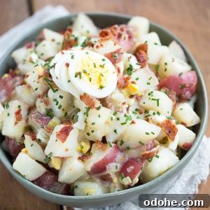 Authentic German Potato Salad with Hard-Boiled Eggs & Bacon 14 German potato salad with hard boiled eggs and chives in a green bowl on a wooden table