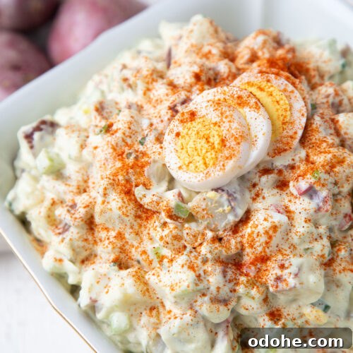 red potato salad topped with hard boiled eggs and paprika in a white dish.