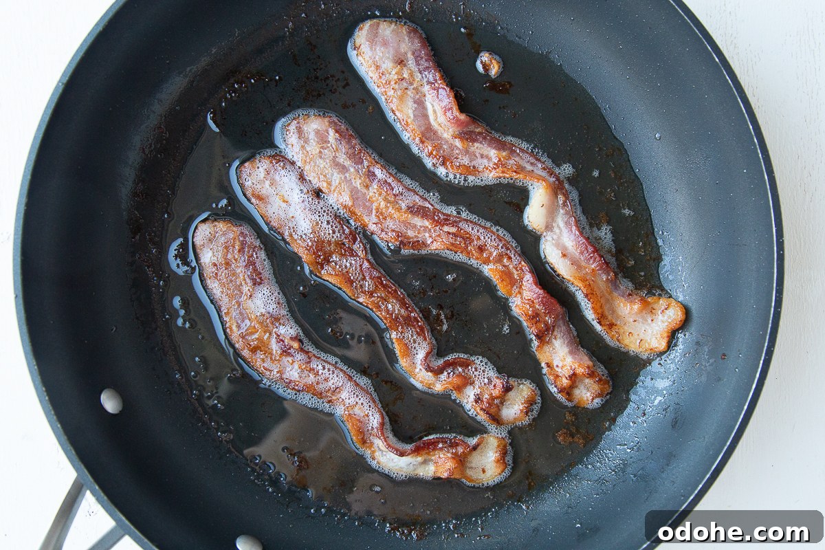 Authentic German Potato Salad with Hard-Boiled Eggs & Bacon 7 four slices of bacon cooking in a nonstick skillet
