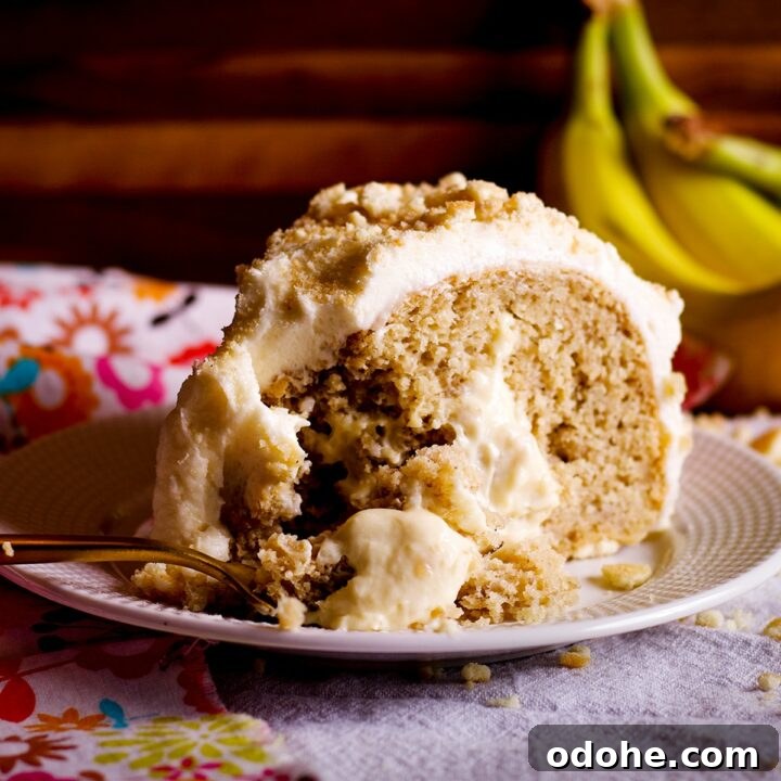 A slice of banana cream cake on a white plate with a bunch of bananas in the background. A gold fork is cutting a bite from the slice of cake.