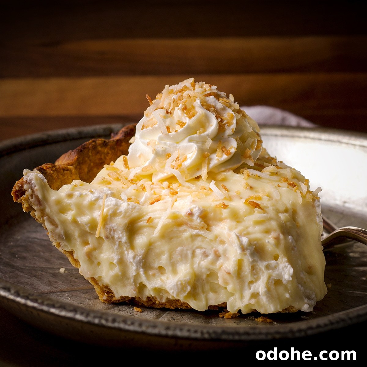 A slice of coconut cream pie on a tin plate.