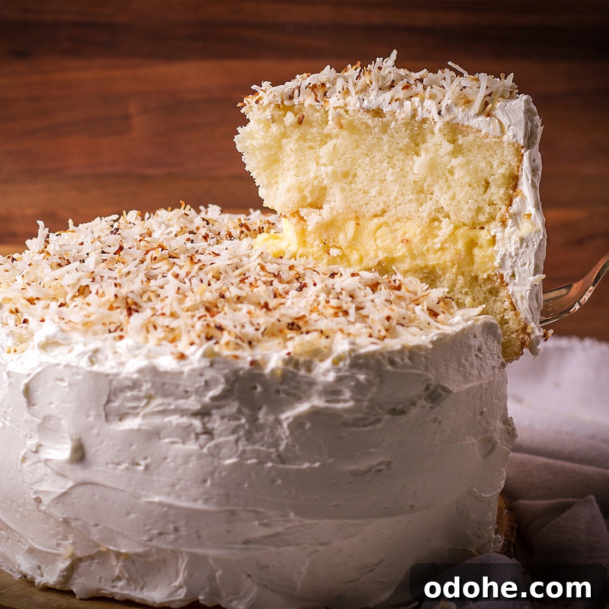 Someone using a cake server to lift a slice of coconut cream cake from the whole cake.