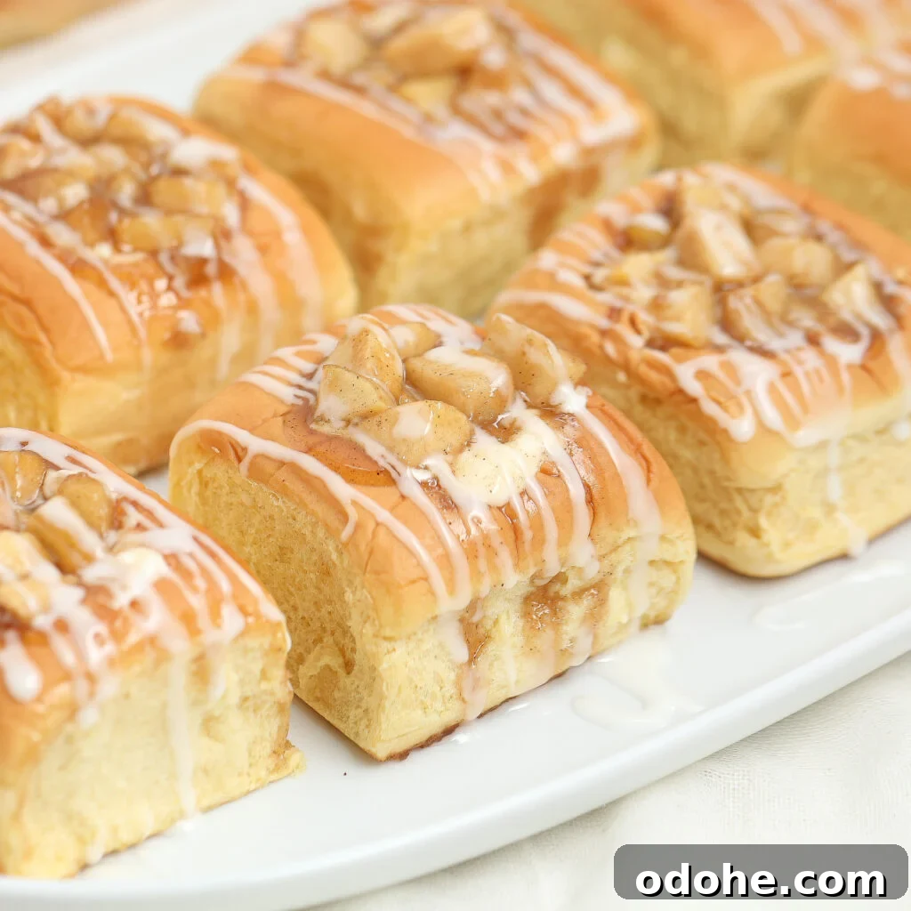 Golden brown danishes topped with chopped nuts and drizzled with white icing are arranged on a white rectangular plate.