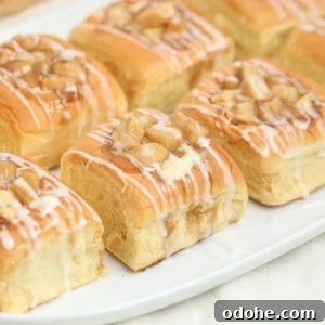 Golden brown danishes topped with chopped nuts and drizzled with white icing are arranged on a white rectangular plate.