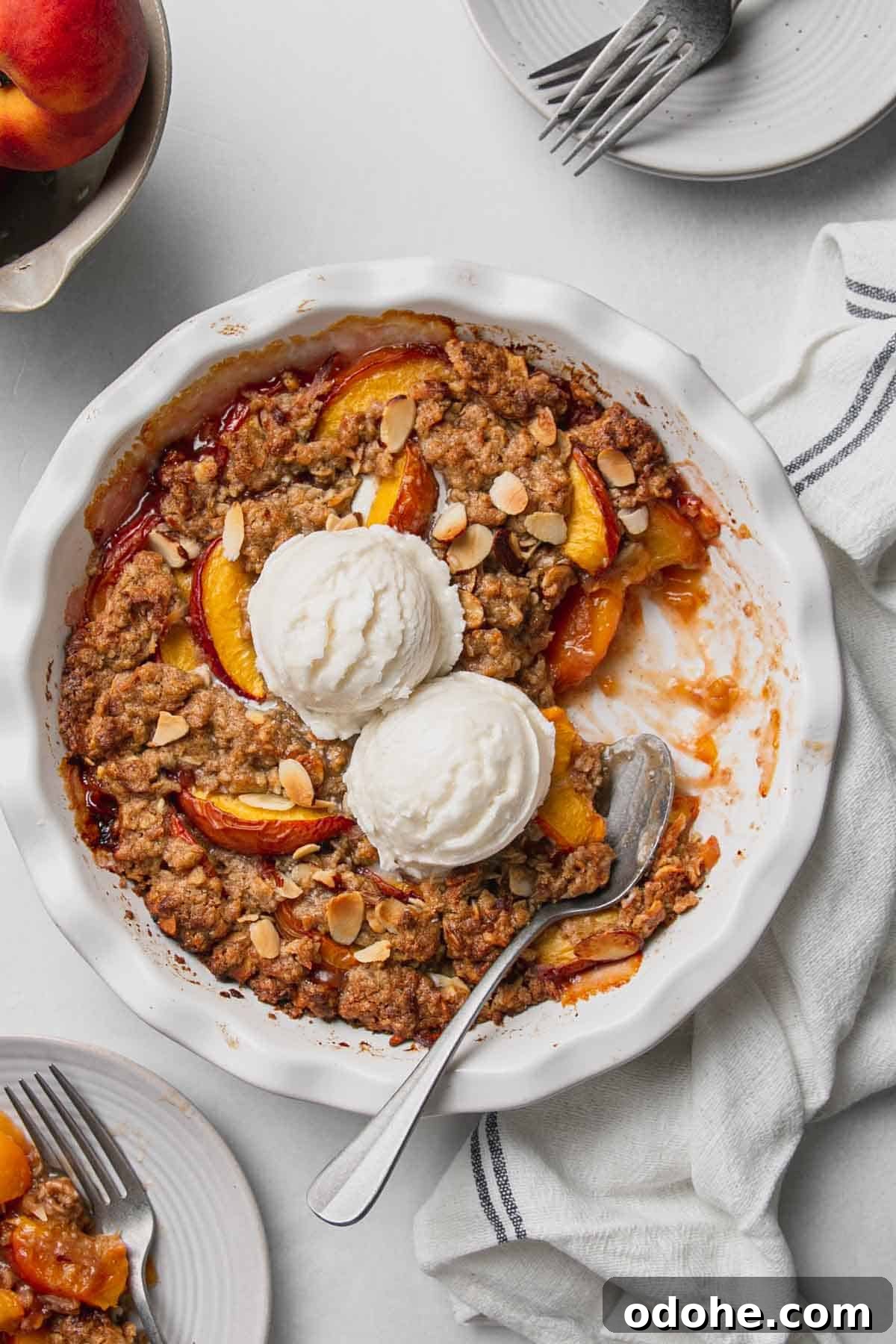 Gluten-Free Peach Crisp with Oats & Almonds — Simple Summer Dessert 2 Gluten-free Peach Crisp in a white pie dish with scoop removed and two scoops of ice cream on top.