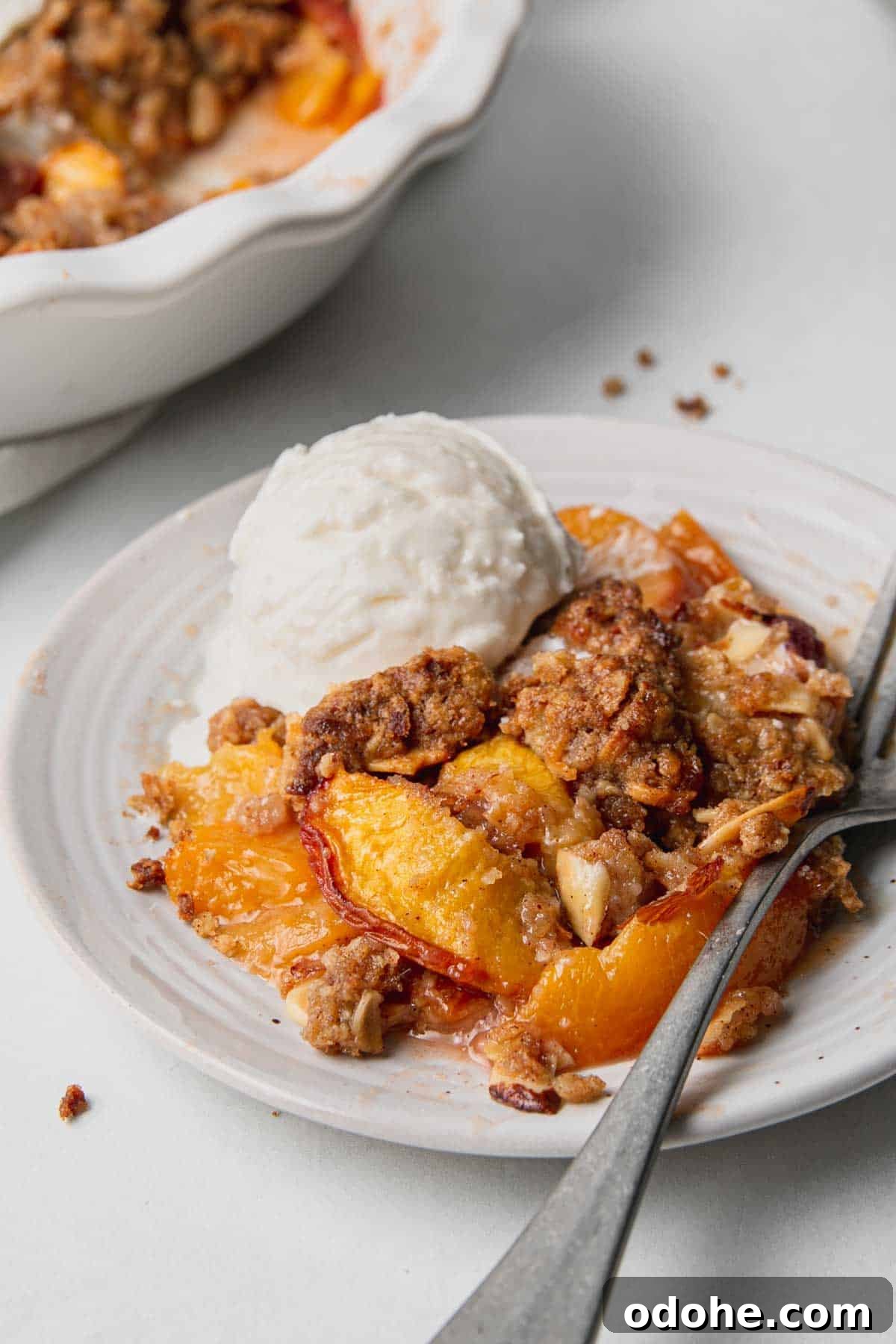 Gluten-Free Peach Crisp with Oats & Almonds — Simple Summer Dessert 7 Pile of peach crisp on plate with a scoop of vanilla ice cream and fork to the side.