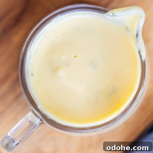 A glass measuring cup filled with creamy yellow sauce, viewed from above, on a wooden surface.