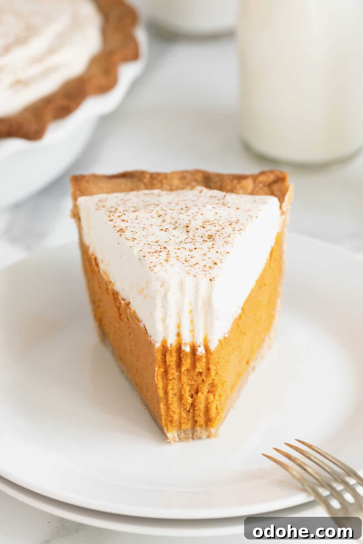 Creamy Pumpkin Pie Recipe: Classic Autumn Dessert Guide 5 A piece of pumpkin cream pie on a small white dessert plate with a bite taken out of it.