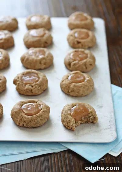 A baking sheet with Salted Caramel Thumbprint Cookies with a bite taken out of one.