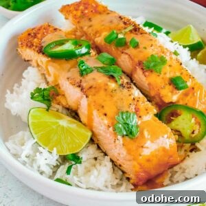Thai-Style Salmon with Coconut Lime Sauce 7 Side close up shot of two pieces of salmon on a bed of rice garnished with parsley and cut jalapeños in a large white bowl with lime wedges on the side.