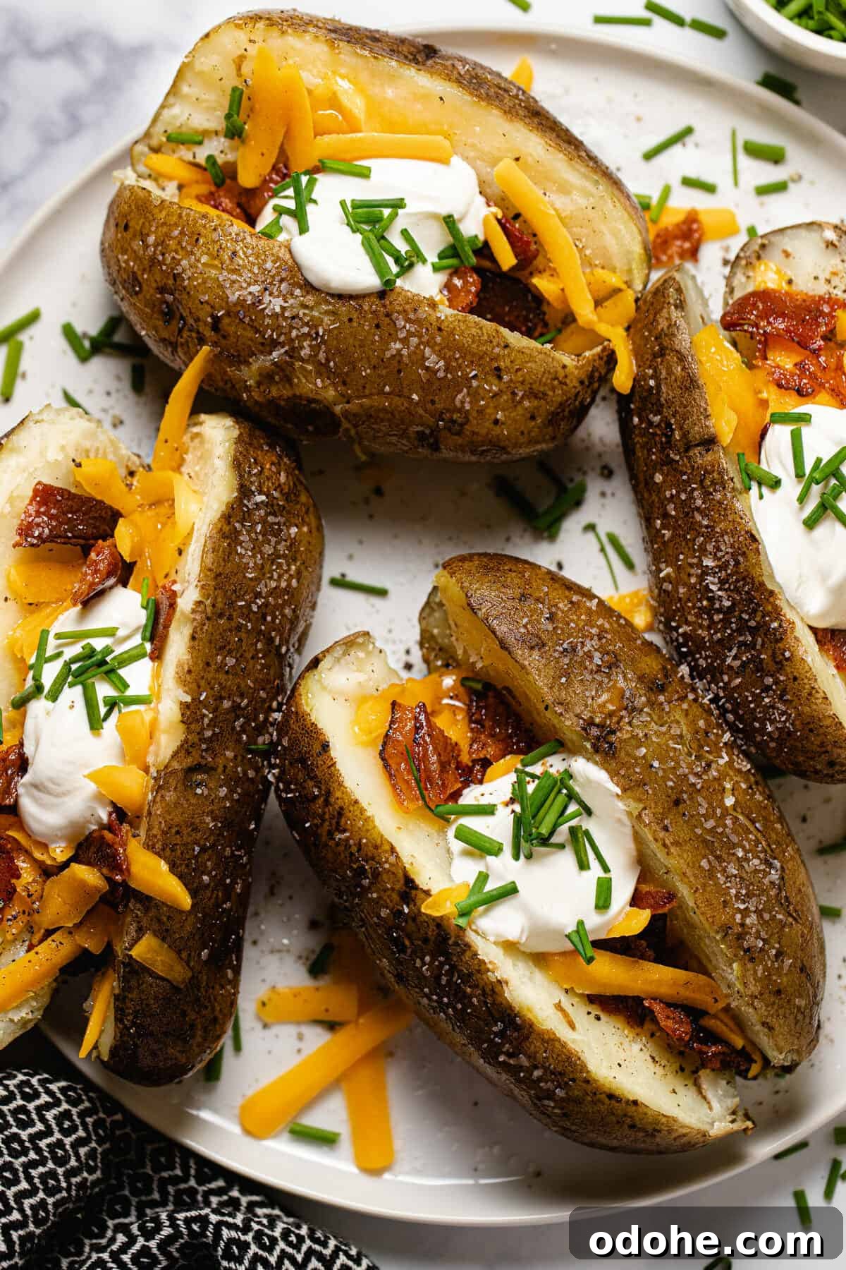 White plate with four loaded baked potatoes garnished with chives