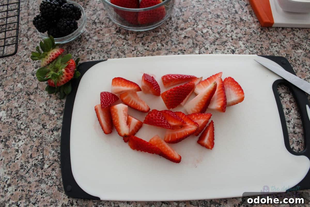 Sliced strawberries on a cutting board with other fruits and the display board partially in frame.