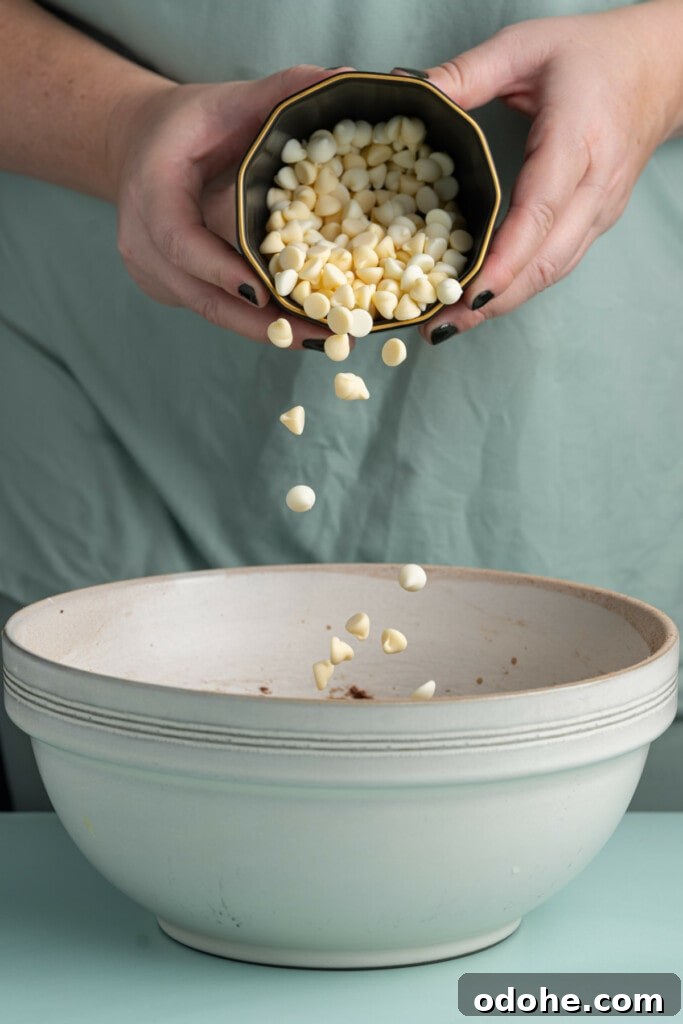 Adding white chocolate chips to cookie dough.