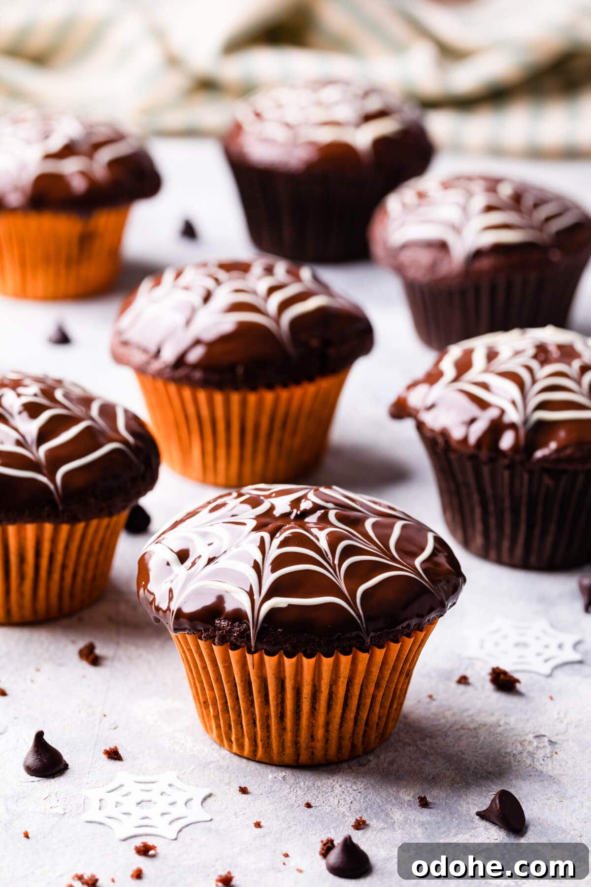 Chocolate Fudge Spiderweb Muffins Recipe — Decadent Halloween Treat 15 chocolate fudge spiderweb muffins in orange muffin cases standing on a light surface.