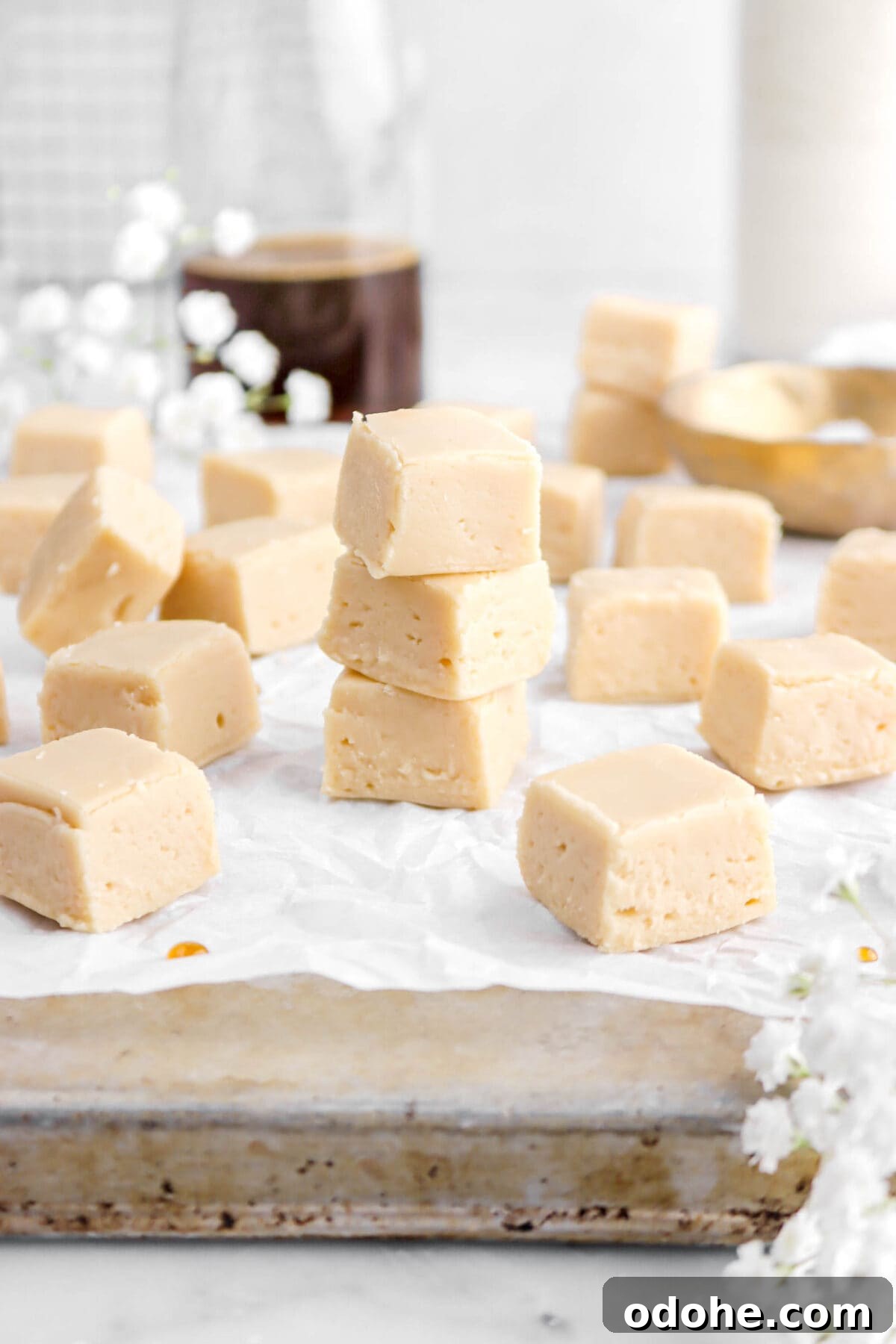 maple fudge stacked on parchment paper lined antique sheet pan with more pieces of fudge around.