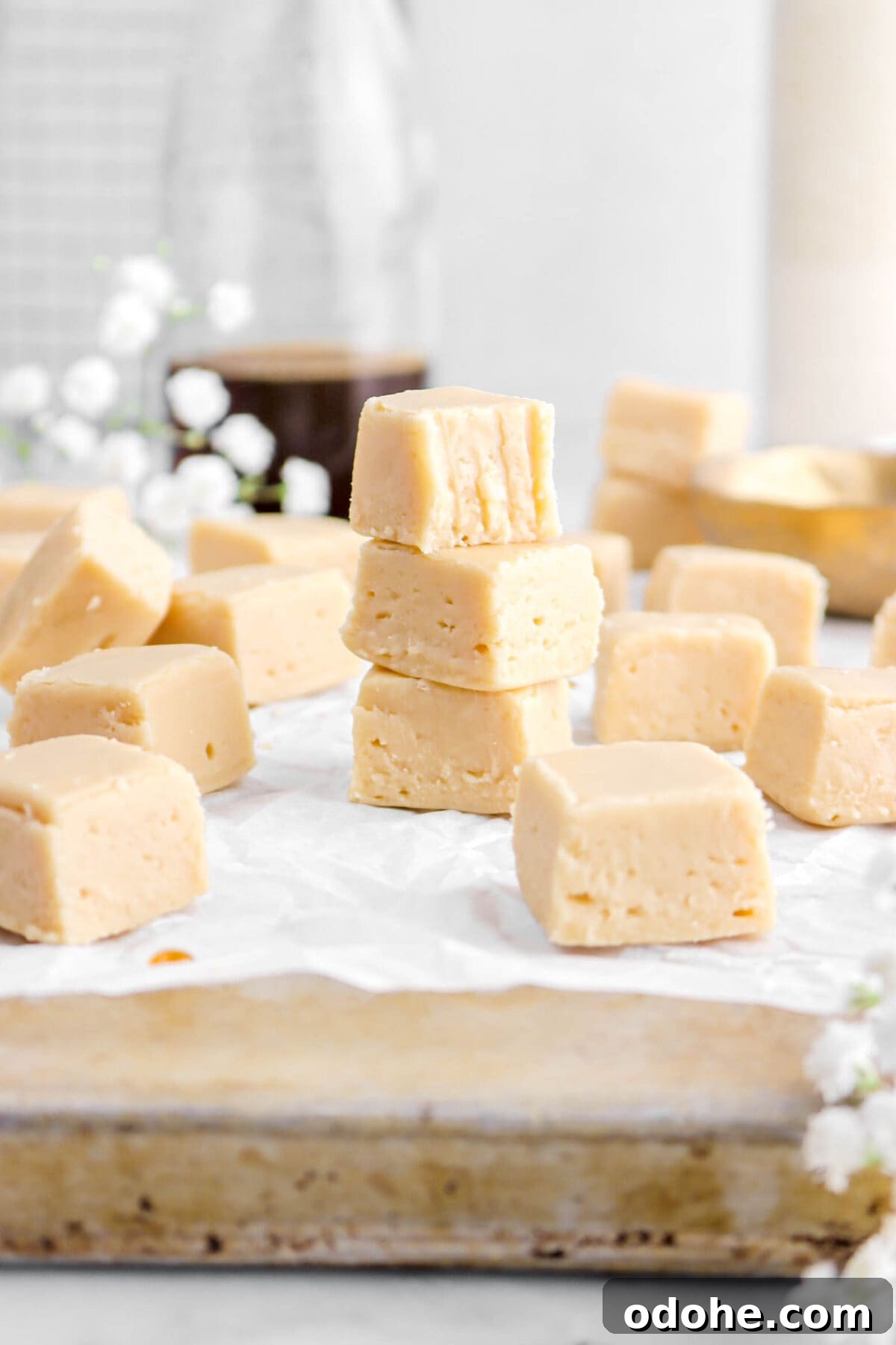 front shot of stacked maple fudge on sheet pan with bite missing out of top piece, more fudge around, and white flowers.