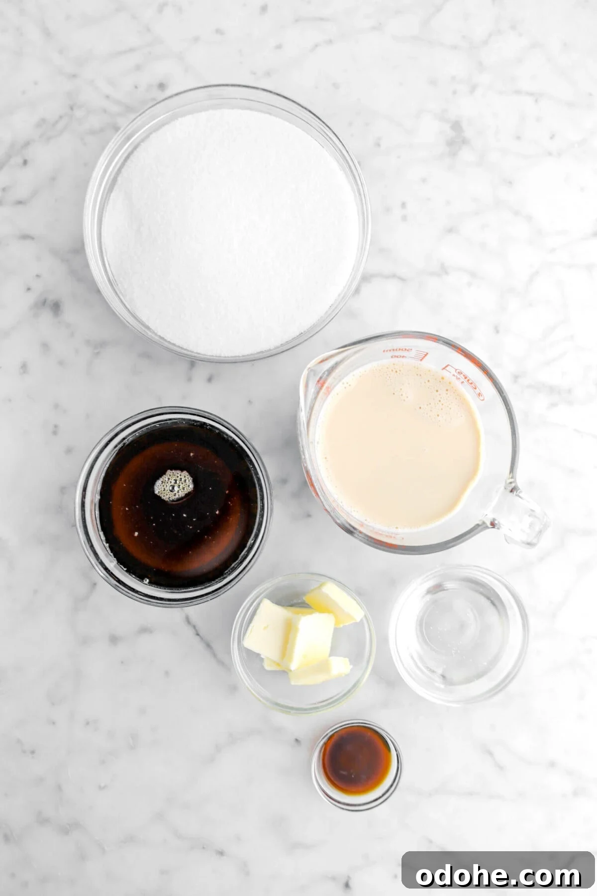 sugar, maple syrup, evaporated milk, butter, corn syrup, and vanilla extract on marble surface.