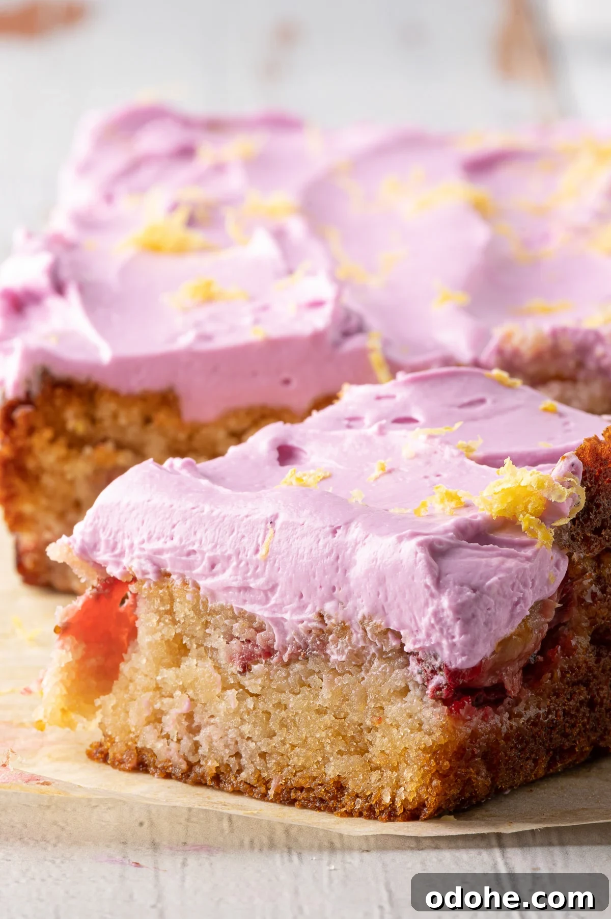 A golden blondie with bits of strawberry and pink icing on a piece of parchment paper