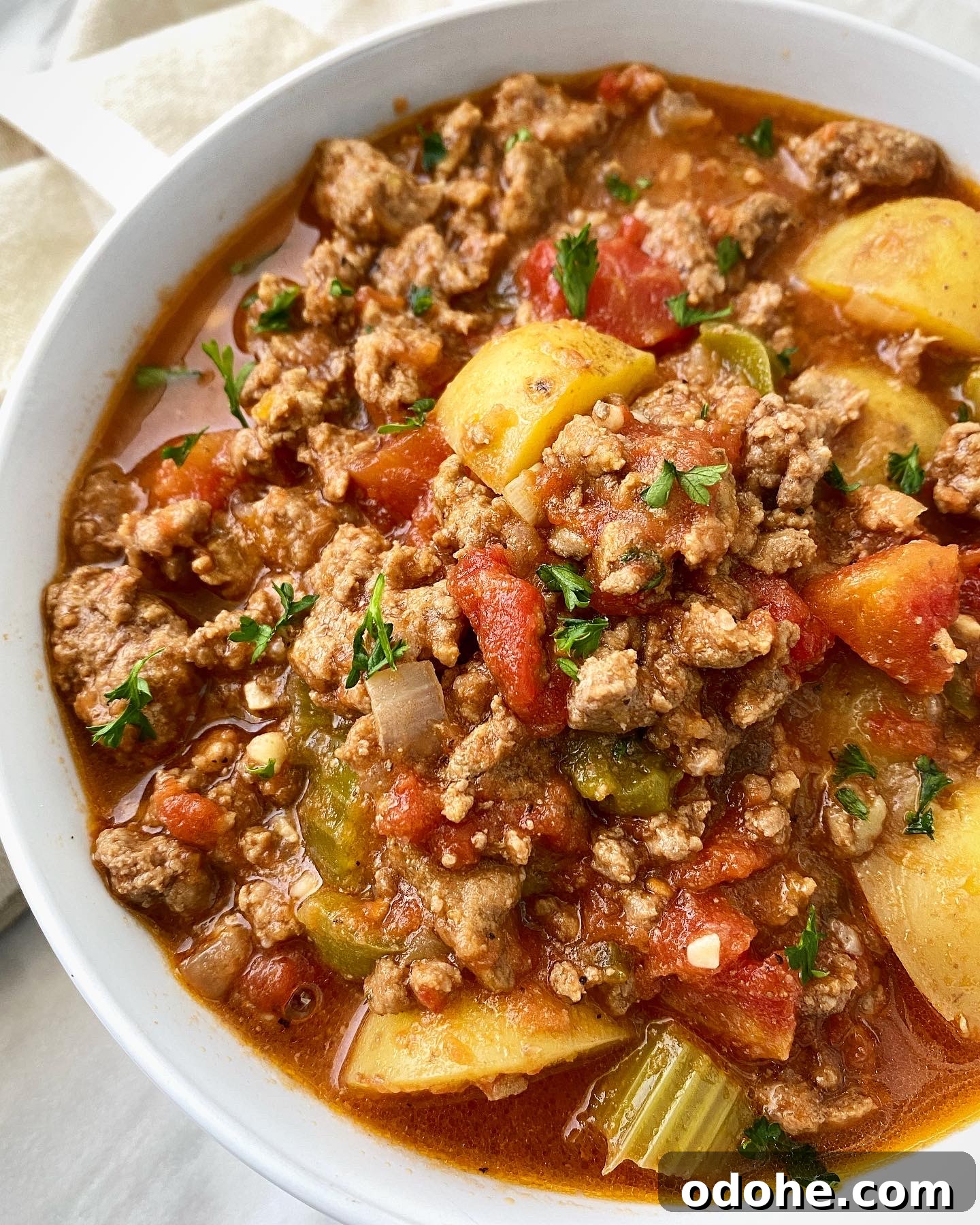 Slow Cooker Hamburger Stew Recipe — Hearty One-Pot Comfort Meal 8 side view shot of hamburger stew in a white bowl garnished with fresh parsley