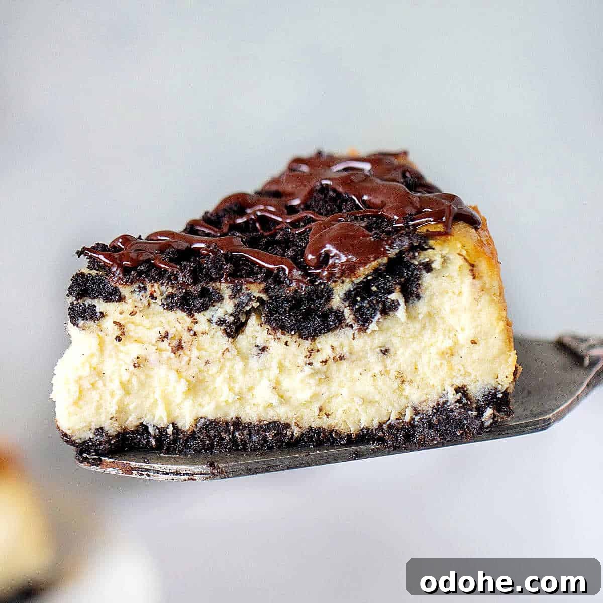 A metal cake server with chocolate topped oreo cheesecake, grey background.