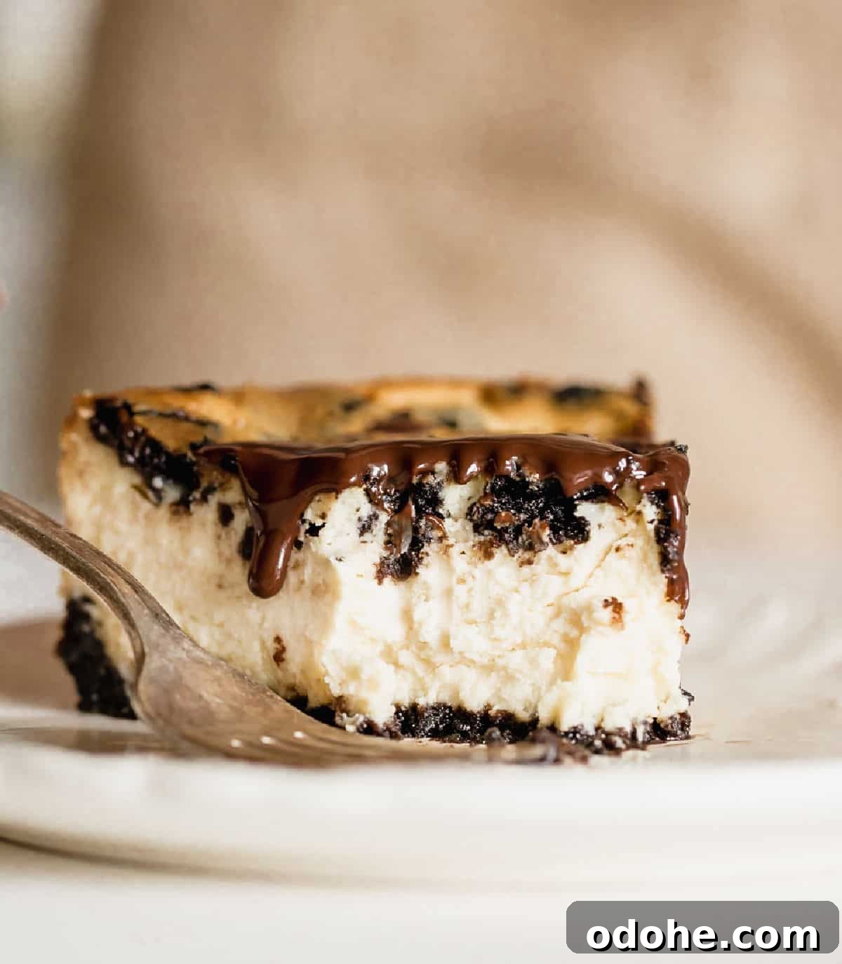 Bitten piece of oreo cheesecake on white plate with fork.