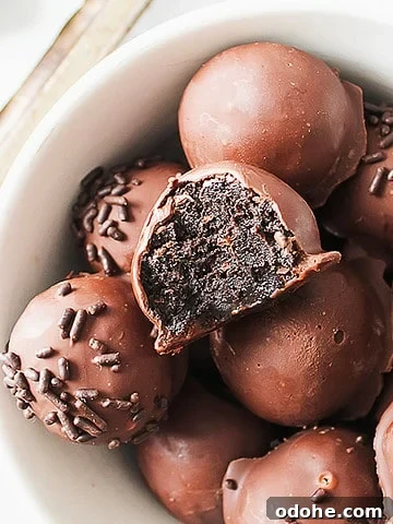 Bitten chocolate-covered Oreo truffle over several whole more in a white bowl.