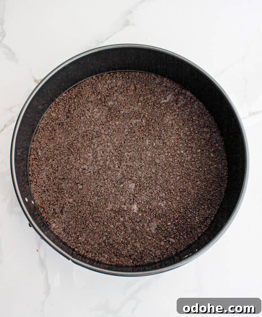 Top view of dark round cake pan with Oreo crust. White marbled surface.