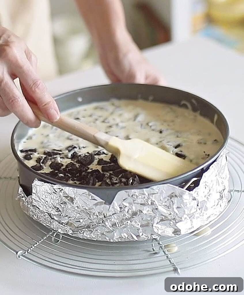 Submerging oreo pieces on cheesecake batter with a yellow spatula. White surface.