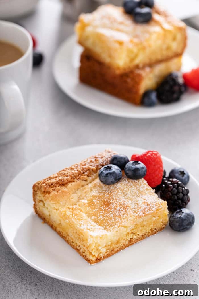 Slice of gooey butter cake on a white plate, garnished with fresh berries.