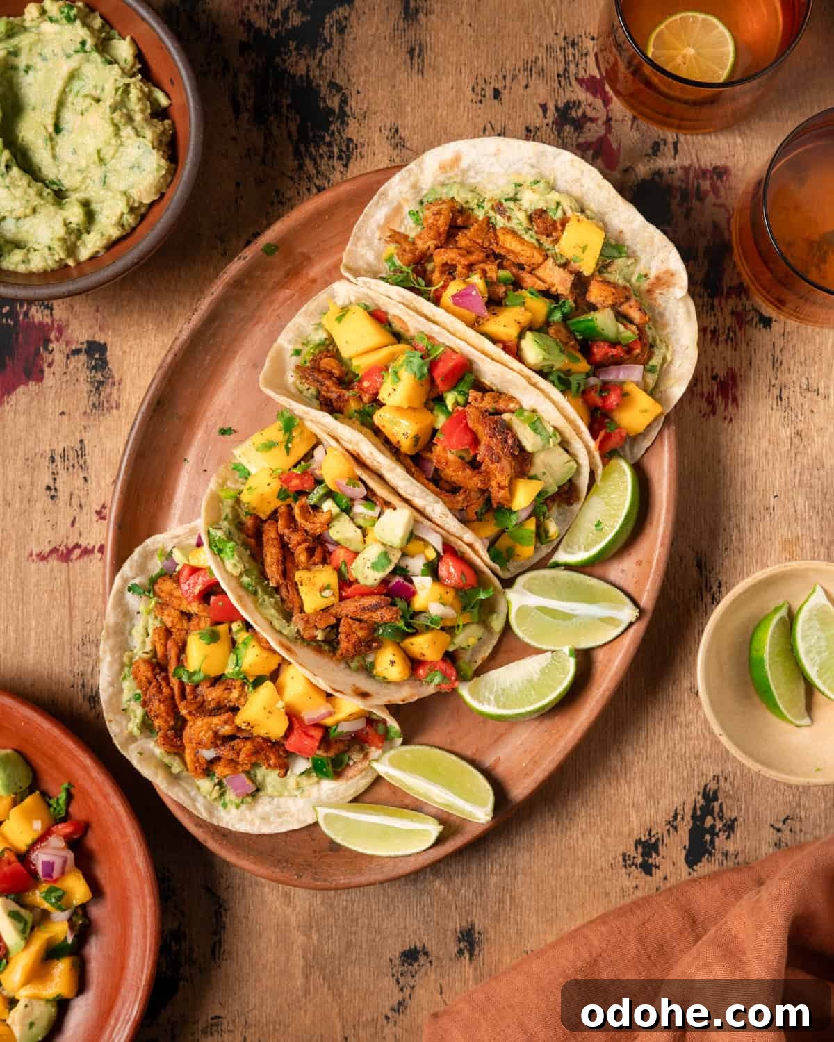 a table with four vegan tacos on a large plate next to ingredient bowls.