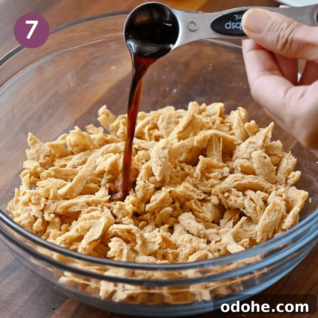 Person pouring tamari into the soy curls in a bowl,