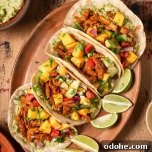 Flatlay of four vegan tacos with soy curls and mango salsa on wooden table.