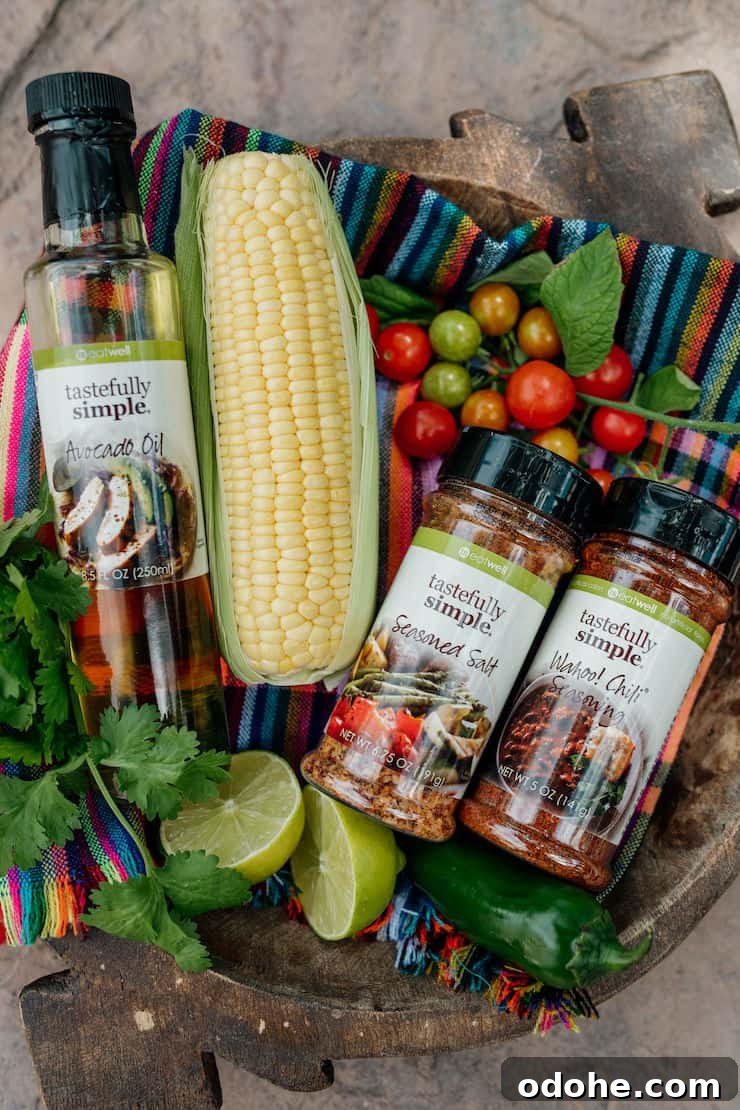 Corn on the cob, fresh limes, jalapeños, and grape tomatoes arranged with avocado oil, seasoned salt, and chili powder—ingredients for Mexican Street Corn Salad.