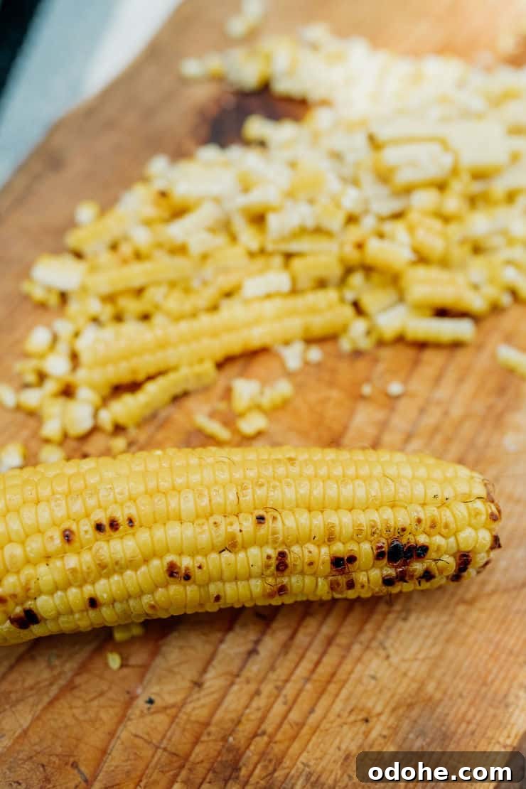 Charred corn on the cob partially sliced on a wooden cutting board, ready to be turned into Mexican Street Corn Salad.