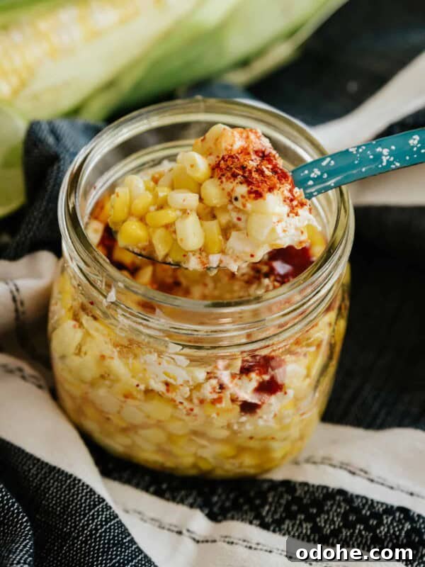 Short mason jar filled with elote en vaso (a.k.a. esquites), topped with chili powder and cotija cheese.