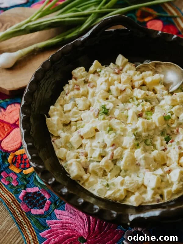 Texas-style potato salad recipe by Yvette Marquez-Sharpnack of Muy Bueno, served in a black bowl with eggs, mustard, and pickles on a wooden table