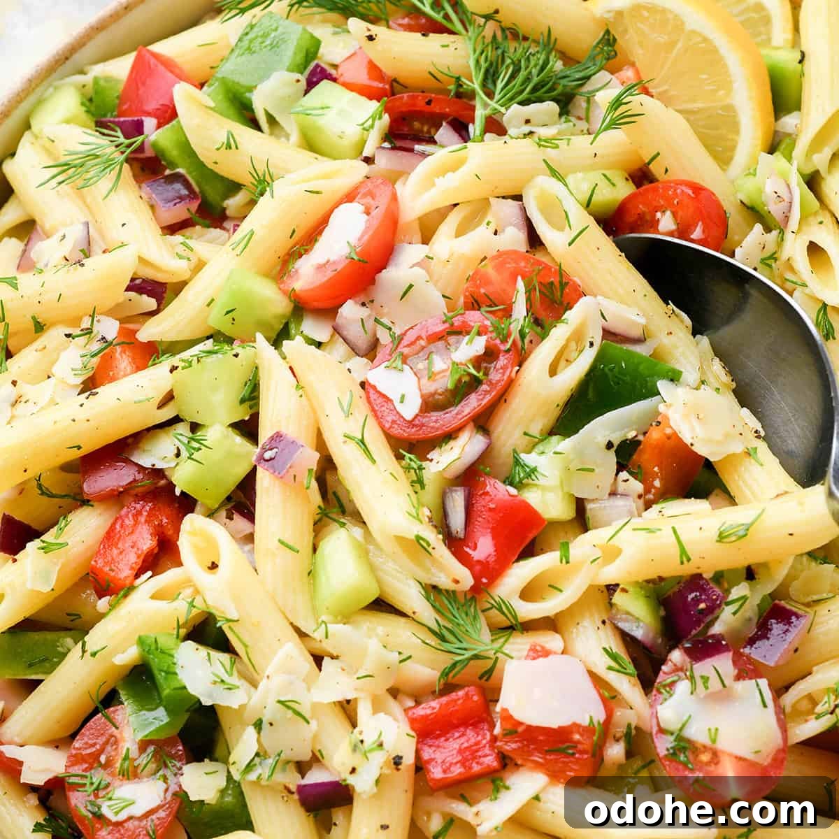 Zesty Lemon Pasta Salad with Fresh Herbs and Creamy Dressing 12 close up photo of a spoon taking a scoop of lemon pasta salad with penne pasta, fresh dill, tomatoes, cucumbers and slices of lemon in a large ceramic bowl