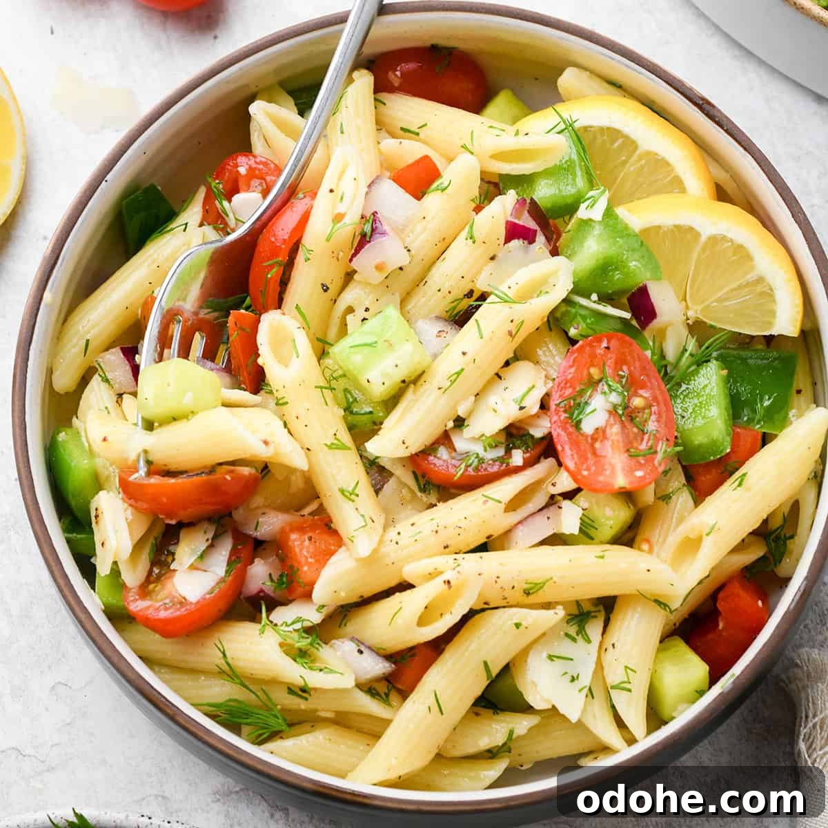 Zesty Lemon Pasta Salad with Fresh Herbs and Creamy Dressing 5 lemon pasta salad with penne pasta, fresh dill, tomatoes, cucumbers and slices of lemon in a small bowl with a fork