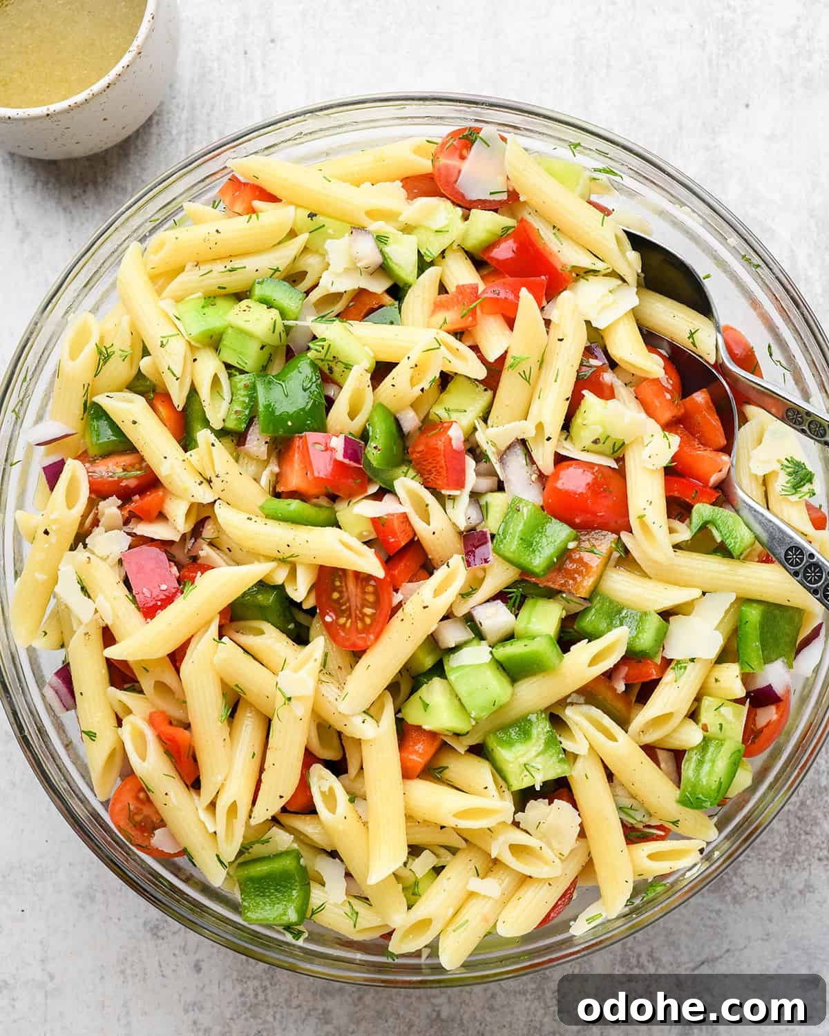 Zesty Lemon Pasta Salad with Fresh Herbs and Creamy Dressing 9 lemon pasta salad being stirred together in a large bowl with penne pasta, fresh dill, tomatoes, cucumbers and bell peppers