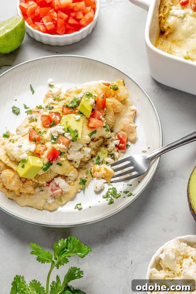 Creamy Shrimp Enchiladas Recipe 2 enchiladas topped with cheese, tomatoes and avocado on plate with fork