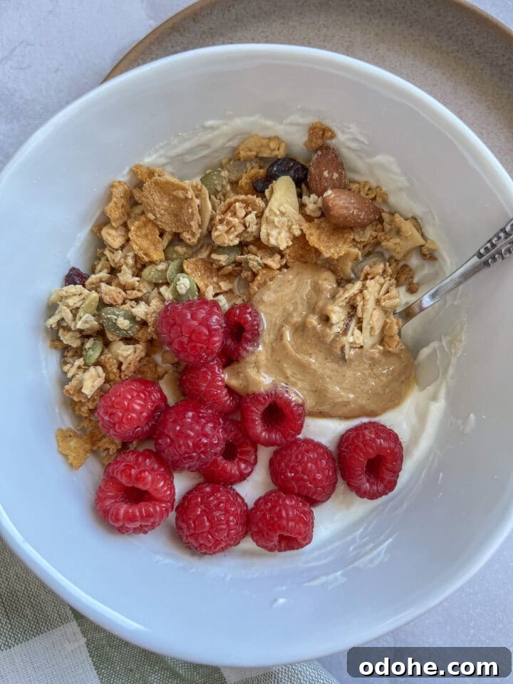 High protein yogurt bowl in a white bowl, topped with nut butter, raspberries, and granola.