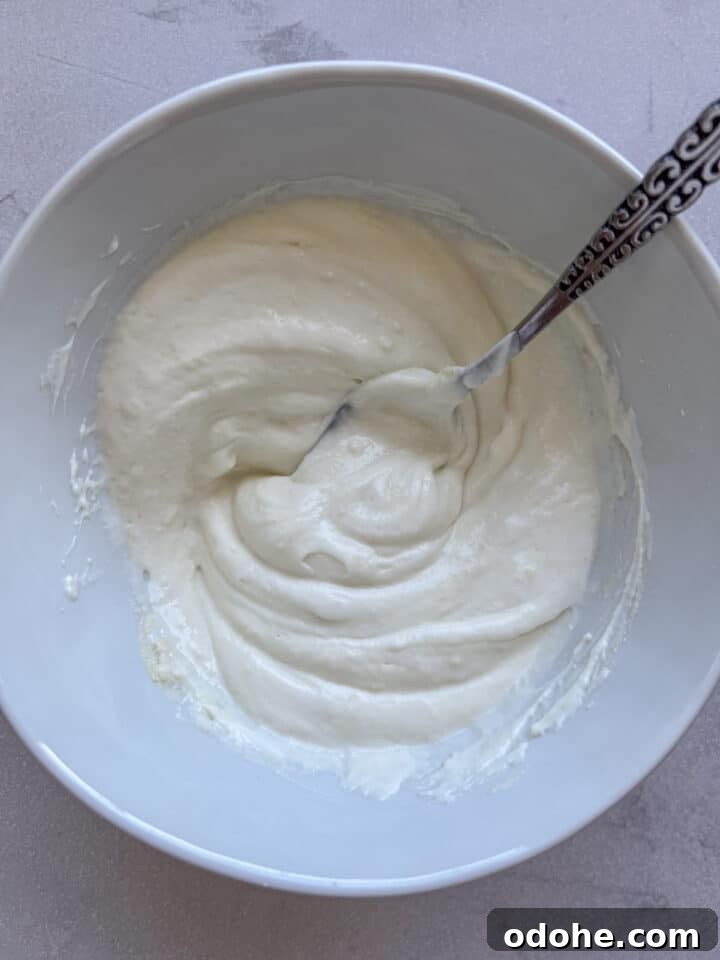 The base of a high protein yogurt bowl in a white bowl with a spoon, just greek yogurt and protein powder mixed together.