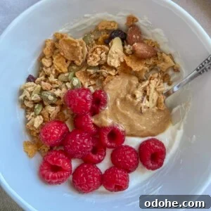 high protein yogurt bowl in a white bowl, topped with raspberries, peanut butter, and granola