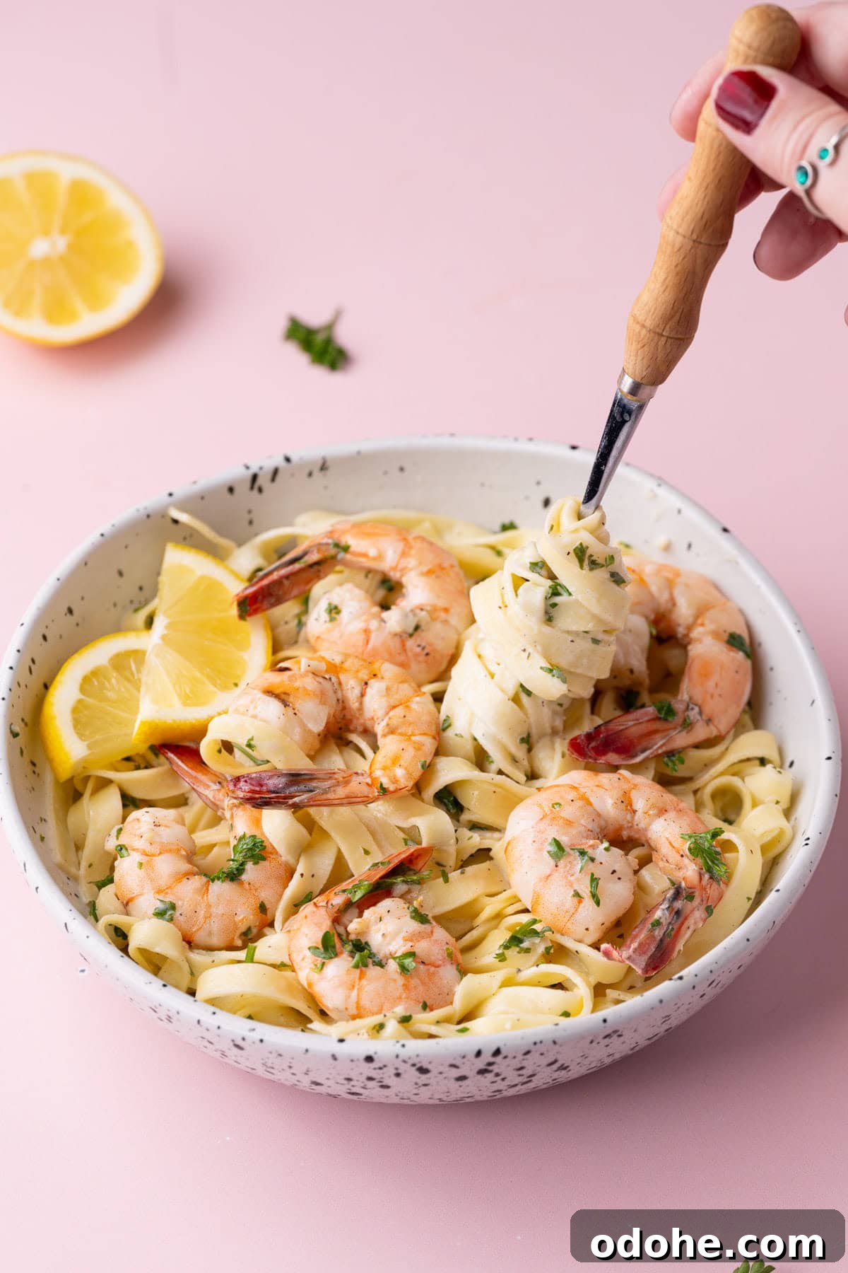 Creamy One-Pan Shrimp Scampi Recipe for Quick Weeknight Dinners 14 Twirling creamy fresh shrimp pasta on a fork with lemon wedges and a halved lemon in the background.
